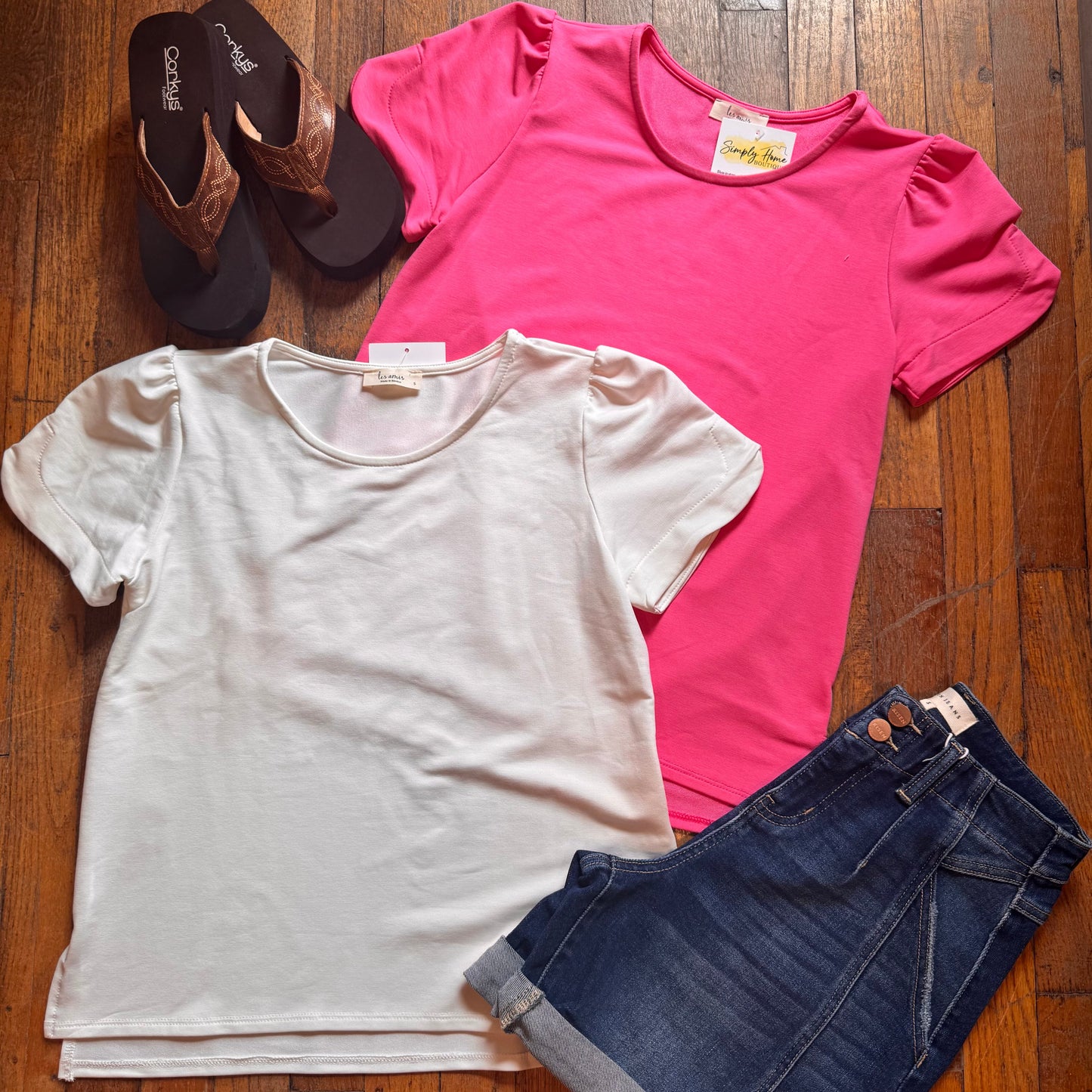 Two t-shirts, a pair of shorts, and sandals on a wooden surface