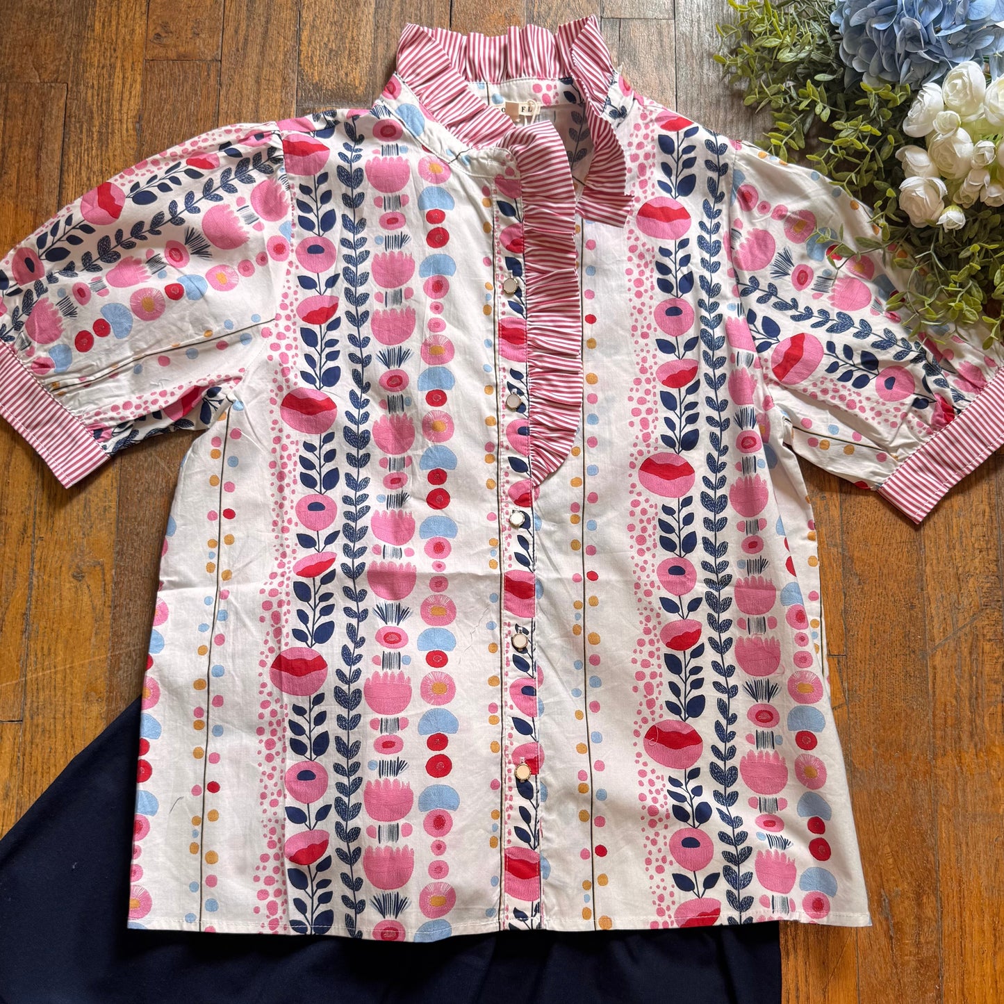Floral patterned shirt on a wooden surface with flowers in the background