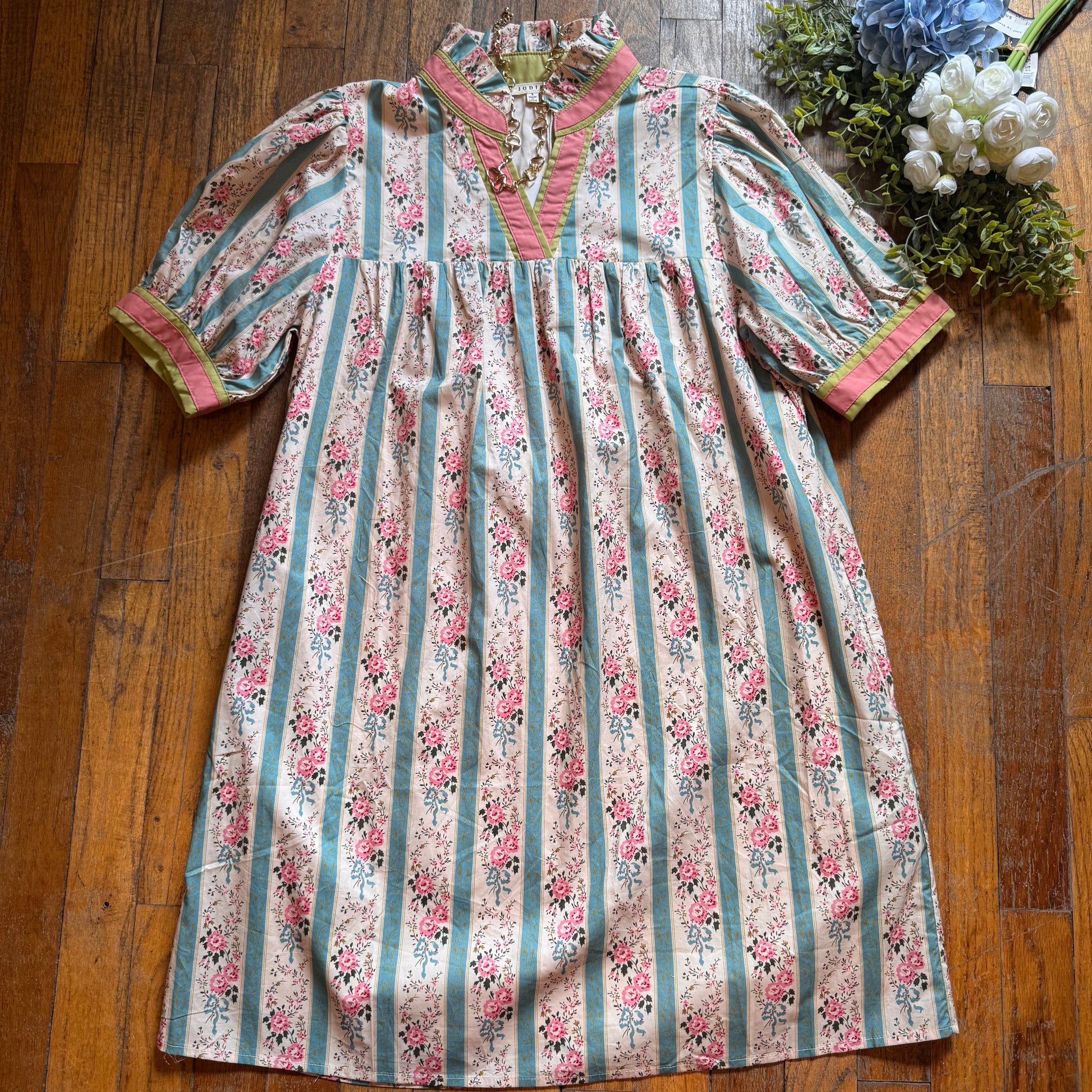 Floral and striped dress on a wooden floor with decorative plants.