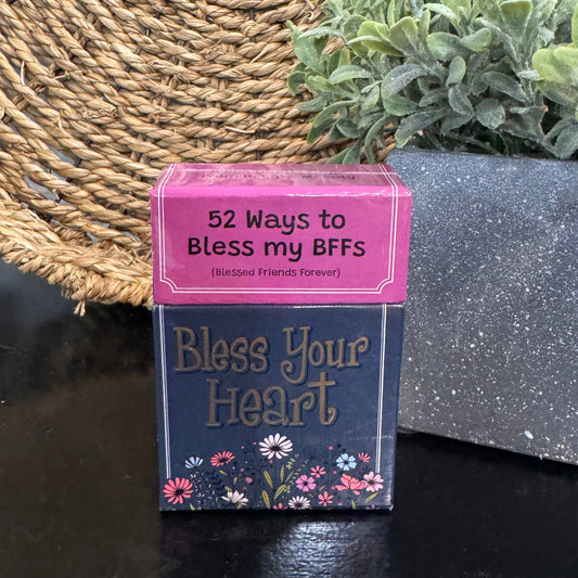 Card game box titled 'Bless Your Heart' with a pink lid on a dark surface.
