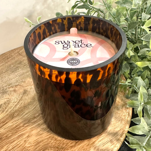 Candle in a leopard print container with 'sweet glace' branding on a wooden surface with plants in the background.