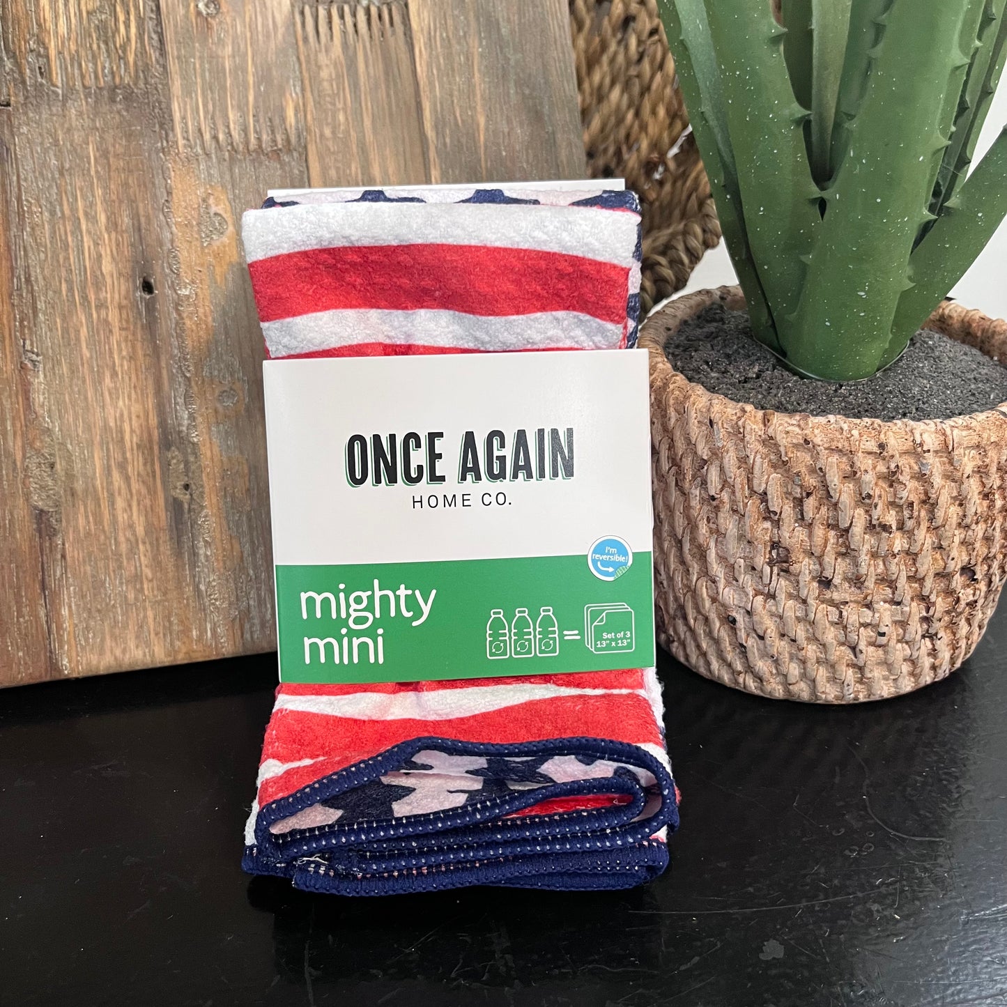 Folded blanket with 'Once Again Home Co.' branding next to a potted cactus on a wooden surface.
