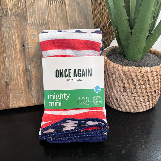 Folded blanket with 'Once Again Home Co.' branding next to a potted cactus on a wooden surface.