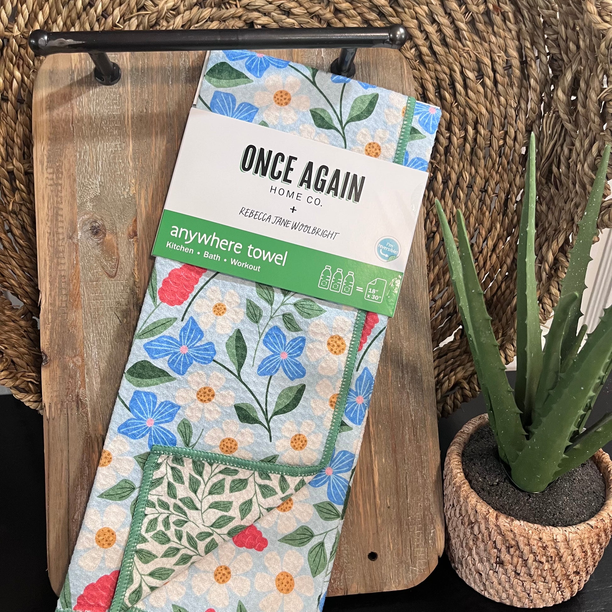 Floral towel packaging with 'Once Again Home Co' branding on a wooden surface with a plant.