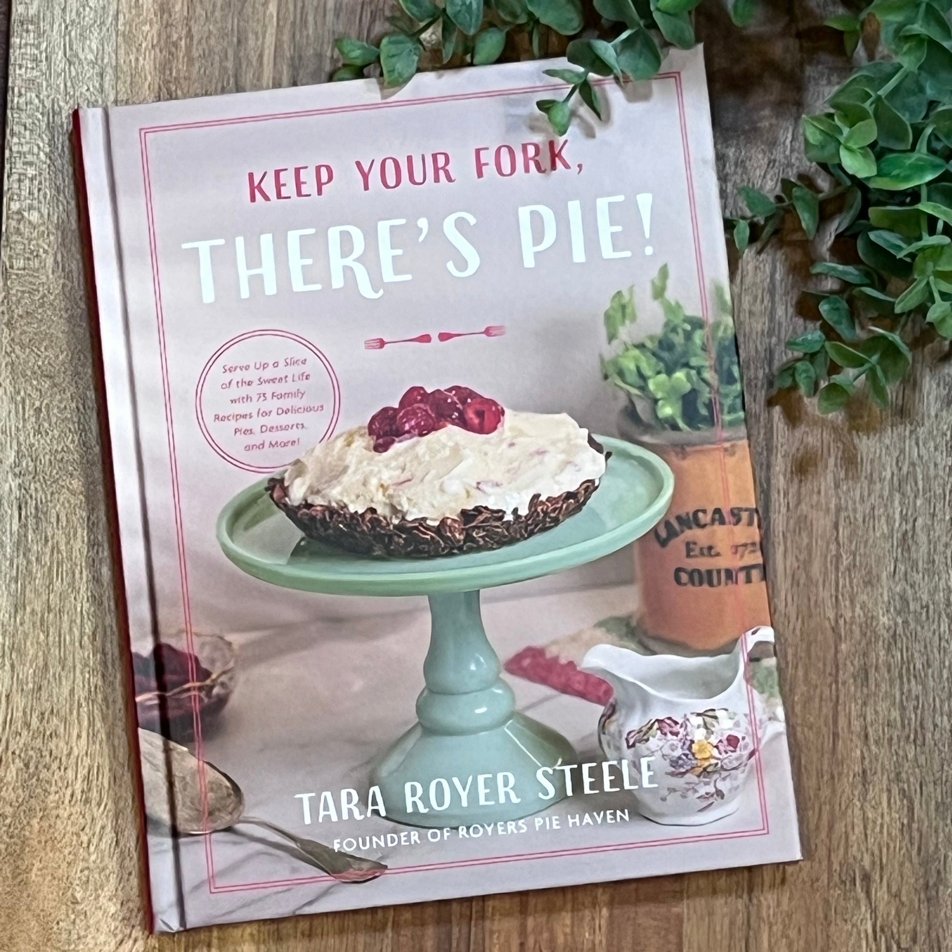 Book with a dessert illustration on a wooden surface with greenery