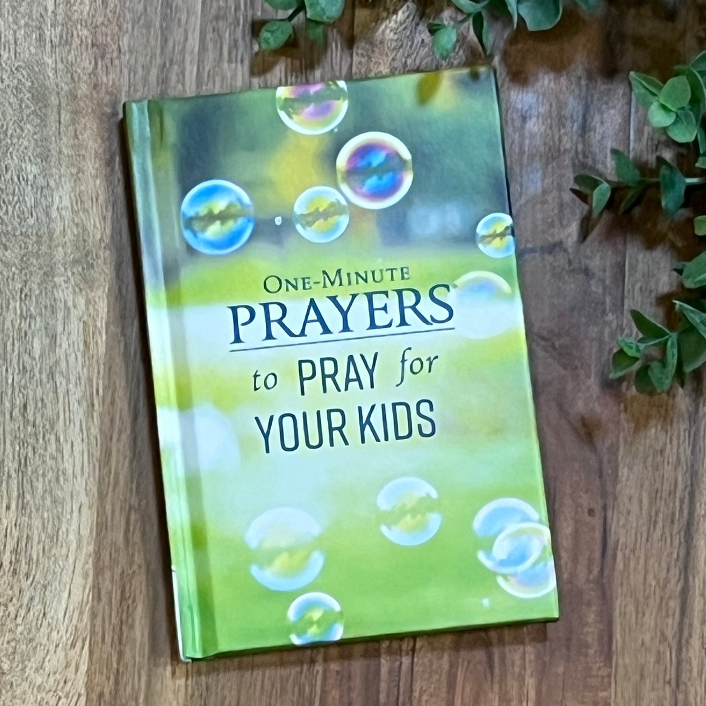 Book titled 'One-Minute Prayers to Pray for Your Kids' on a wooden surface with bubbles on the cover.