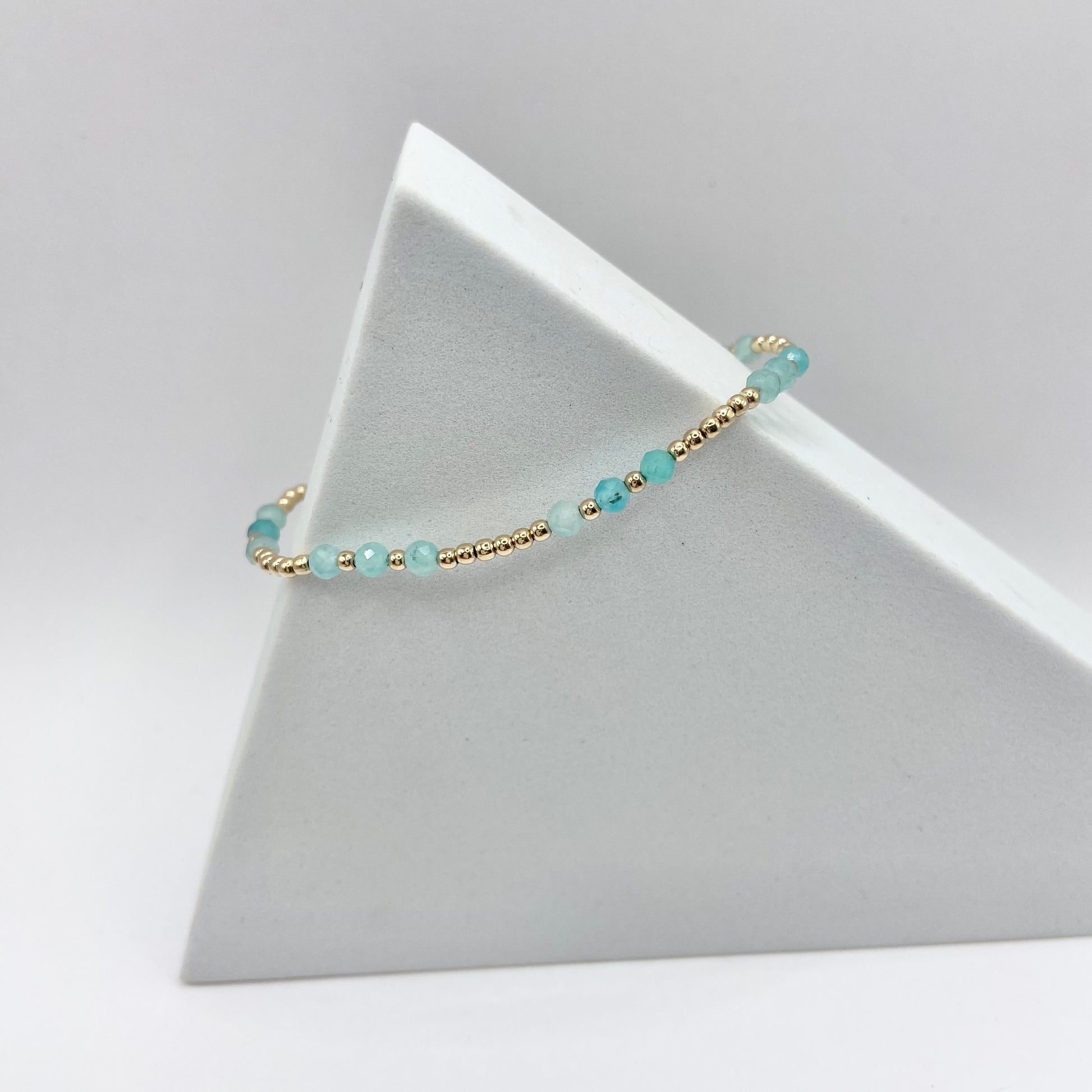 A gemstone bracelet with gold-filled beads and amazonite stones, displayed on a white stand.