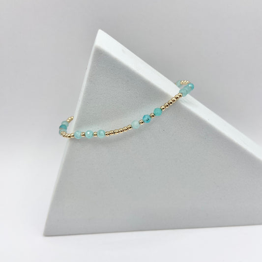 A gemstone bracelet with gold-filled beads and amazonite stones, displayed on a white stand.