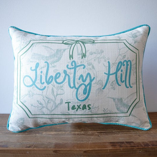 Decorative pillow with 'Liberty Hill, Texas' text on a wooden surface.